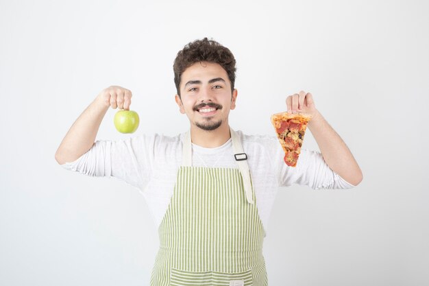 Portrait of smiling male cook showing pizza and green apple on white 