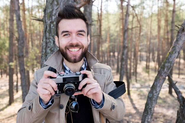 Портрет улыбающегося мужчины турист держит камеру в руке, глядя на камеру