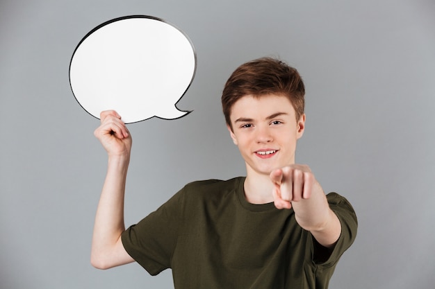 Portrait of a smiling male teenager holding blank speech bubble and pointing finger