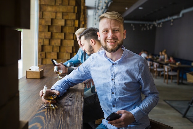 Foto gratuita ritratto dell'uomo sorridente che tiene bicchiere di bevanda nella barra