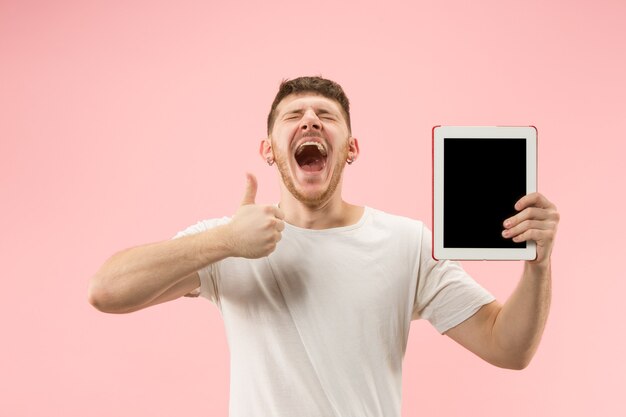 Portrait of smiling man pointing at laptop with blank screen isolated on pink studio background. Human emotions, facial expression concept and advertising concept.