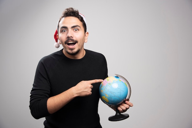 Ritratto di un uomo sorridente con il cappello di babbo natale che punta a un globo.