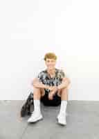 Free photo portrait of smiling man sitting with skateboard against white wall