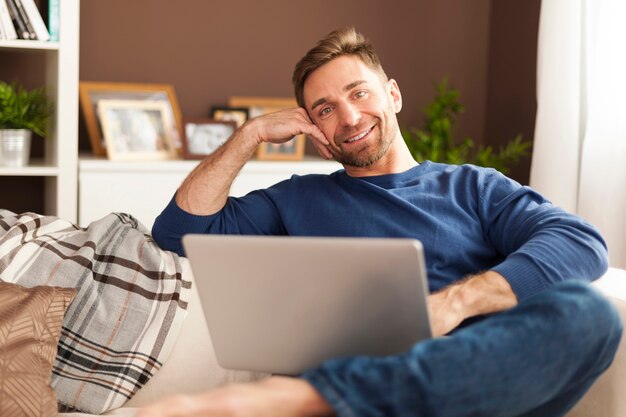 ソファの上のラップトップと笑顔の男の肖像画