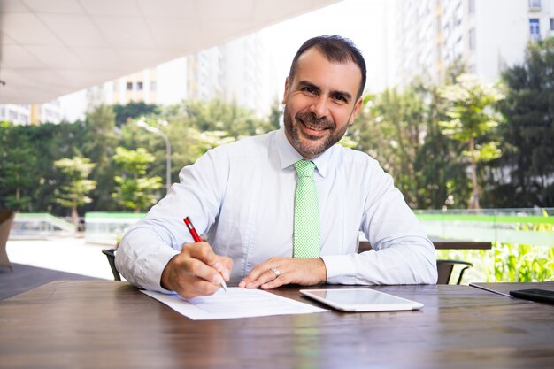 Portrait of smiling mature businessman signing agreement outdoors