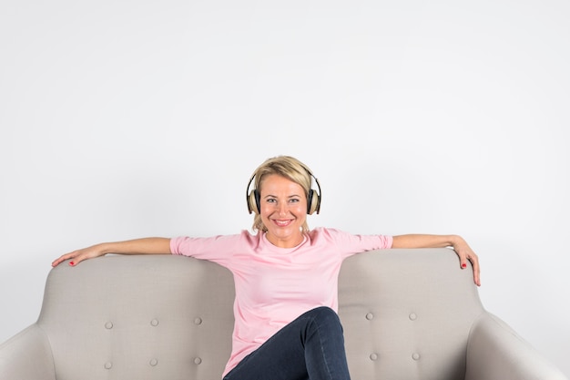 Foto gratuita ritratto di una donna matura sorridente seduto sul divano guardando la telecamera su sfondo bianco