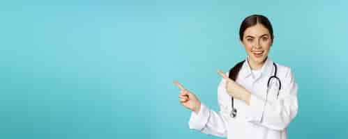 Free photo portrait of smiling medical worker girl doctor in white coat with stethoscope pointing fingers left