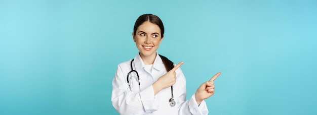 Portrait of smiling medical worker girl doctor in white coat with stethoscope pointing fingers left