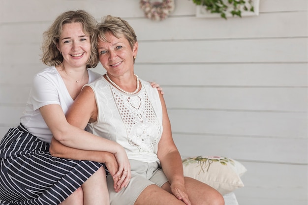 Portrait of smiling mother and daughter sitting on sofa looking at camera