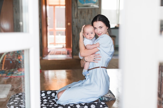 Free photo portrait of smiling mother embracing her baby at home
