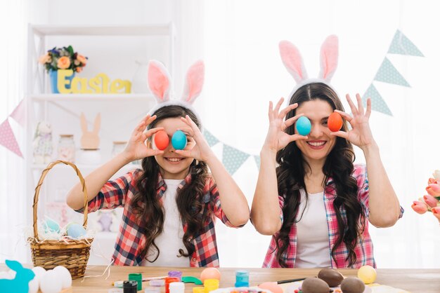 Portrait of smiling mother and her daughter covering their eyes with easter eggs
