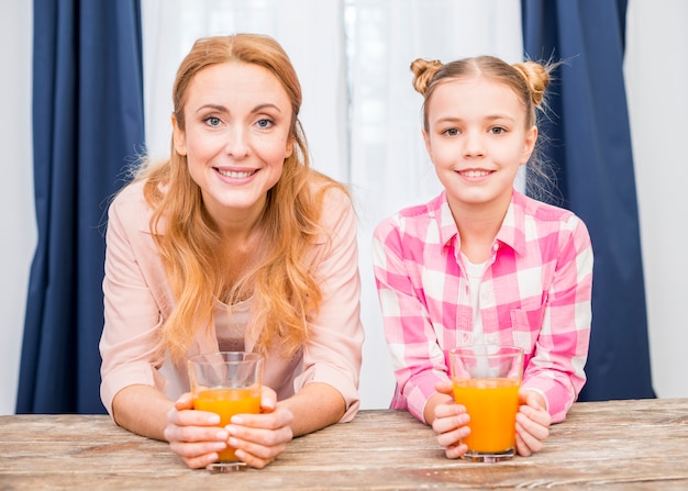 Foto gratuita ritratto di una madre sorridente e sua figlia tenendo il bicchiere di succo guardando la fotocamera