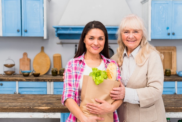 Portrait of smiling mother standing with her daughter holding grocery bag