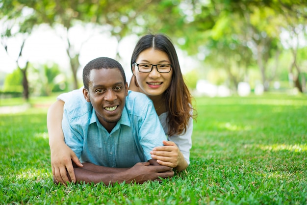 Portrait of smiling multiethnic couple lying on grass in park