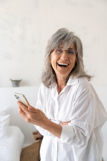 Портрет улыбающейся пожилой женщины, использующей мобильный телефон дома