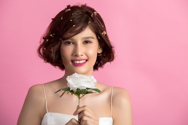 Portrait of a smiling playful cute woman holding flowers isolated on pink