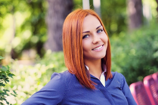 Portrait of smiling redhead female sitting on a bench outdoor.