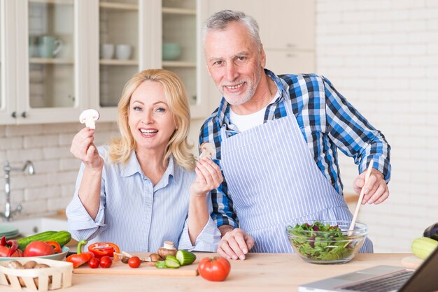 Портрет улыбающиеся старшие пары готовит овощной салат на деревянный стол