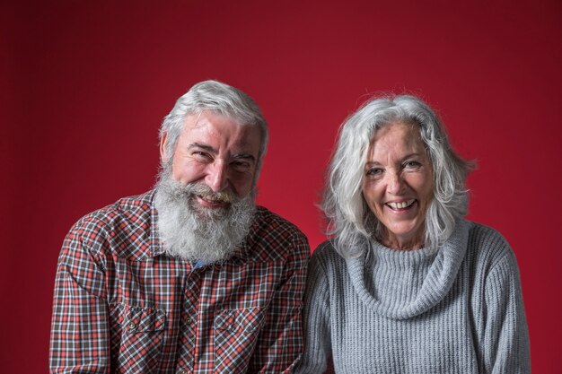 Portrait of smiling senior couple with grey hair against red background