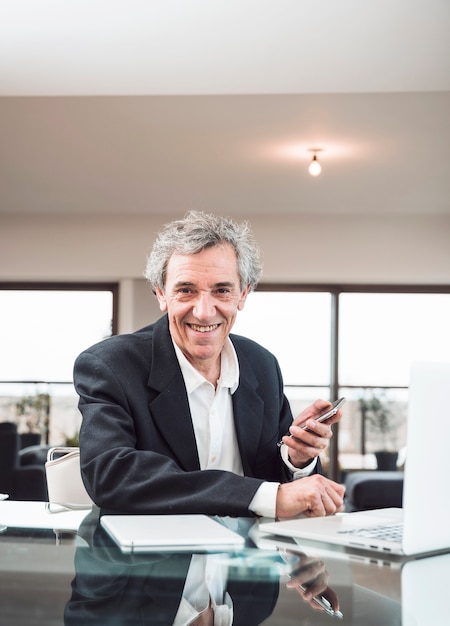 Foto gratuita ritratto dell'uomo senior sorridente con la compressa digitale ed il computer portatile sullo scrittorio riflettente di vetro