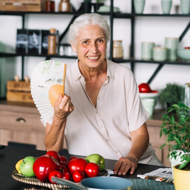 Portrait of smiling senior woman sitting in front of fruits on table