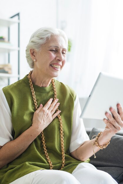 Portrait of smiling senior woman sitting on sofa looking at digital tablet