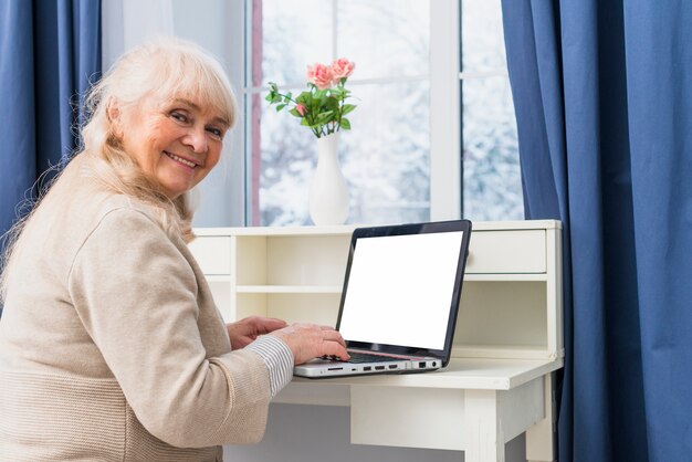 Portrait of a smiling senior woman using laptop with blank white screen