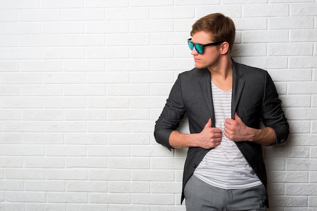 Free photo portrait of smiling stylish man in sunglasses standing against brick wall in modern office.