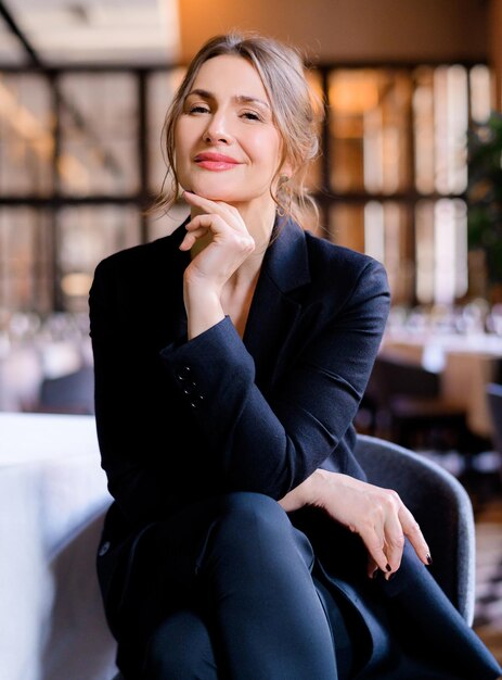 Portrait of smiling successful businesswoman looking into camera sitting in the restaurant Business lady with stylish hairstyle wears elegant suit Business meeting Attractive appearance