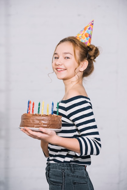 Ritratto di una ragazza sorridente che tiene la torta al cioccolato con candele colorate