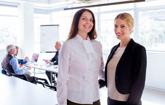 Portrait of smiling two businesswoman standing in front of employees working in the office