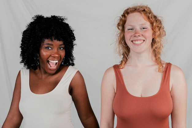 Portrait of smiling two multi ethnic female friends against grey backdrop