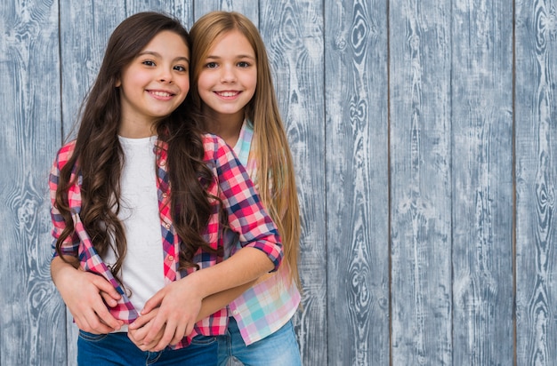 Portrait of smiling two pretty girls standing against grey wooden texture wall