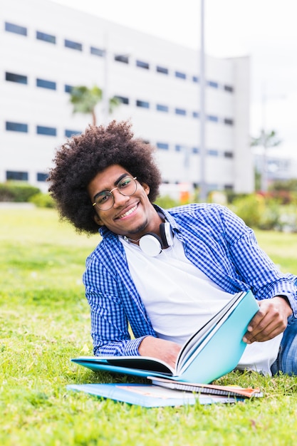 Portrait of smiling university male student holding books in hand lying on campus ground