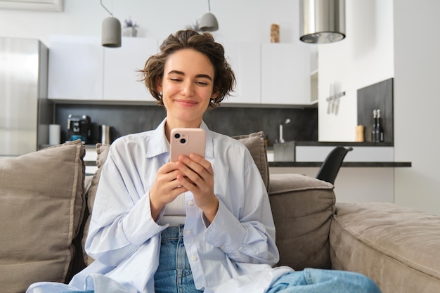 Portrait of smiling woman chats on smartphone app sits at home on sofa and uses mobile phone applica