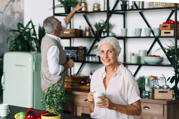 Portrait of smiling woman holding coffee cup sitting in front of man taking bottle from shelf