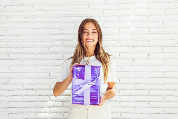 Portrait of a smiling woman holding gift box in front of brick wall