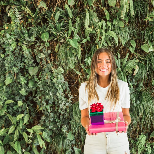 Portrait of a smiling woman holding gift boxes in front of green leaves