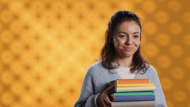 Foto gratuita ritratto di una donna sorridente che tiene una pila di libri facendo il gesto della mano di saluto