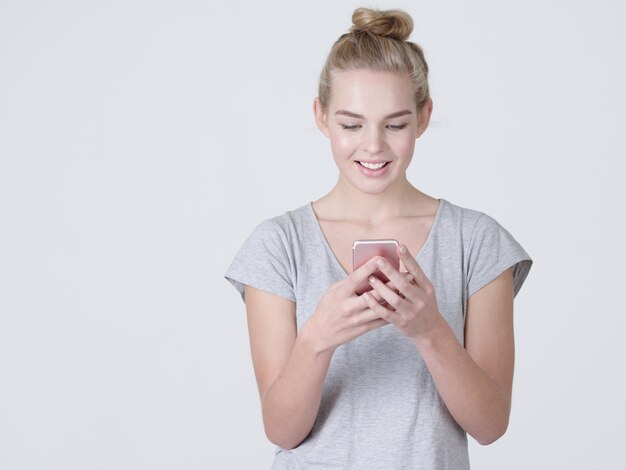 Портрет улыбающейся женщины набирает текстовое сообщение на мобильном телефоне - в студии
