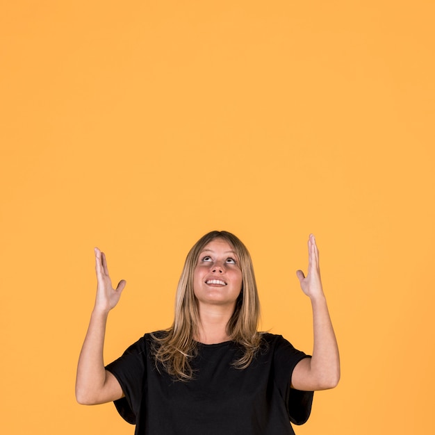 Portrait of smiling woman looking up and gesturing on yellow wall background