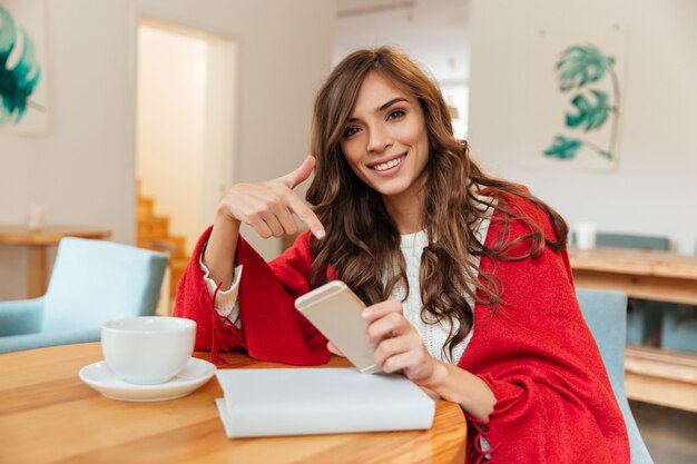Portrait of a smiling woman pointing finger at mobile phone