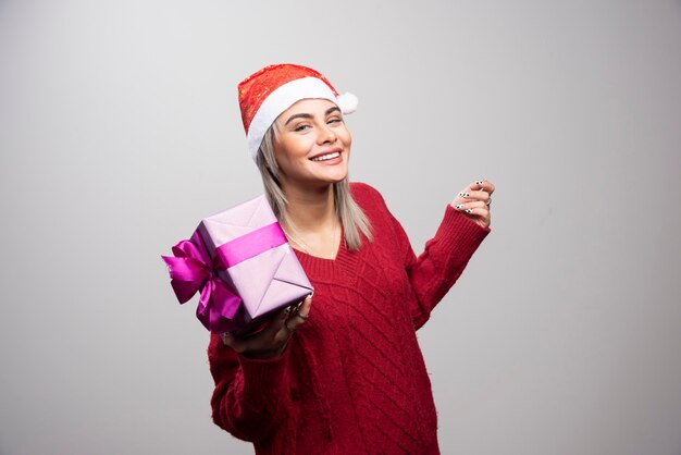 Portrait of smiling woman posing with Christmas gift on gray background.