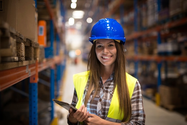 Free photo portrait of smiling woman in protective uniform with hardhat holding tablet in warehouse center