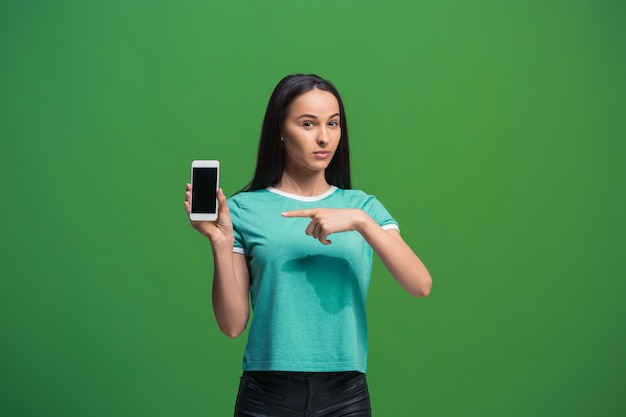 Portrait of a smiling woman showing blank smartphone screen isolated on a green background