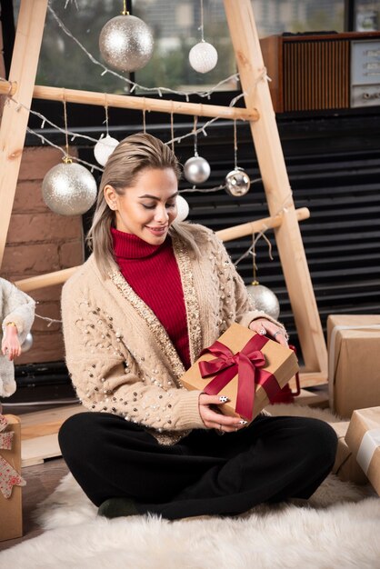 Portrait of a smiling woman sitting on a floor with lots of Christmas gift boxes 