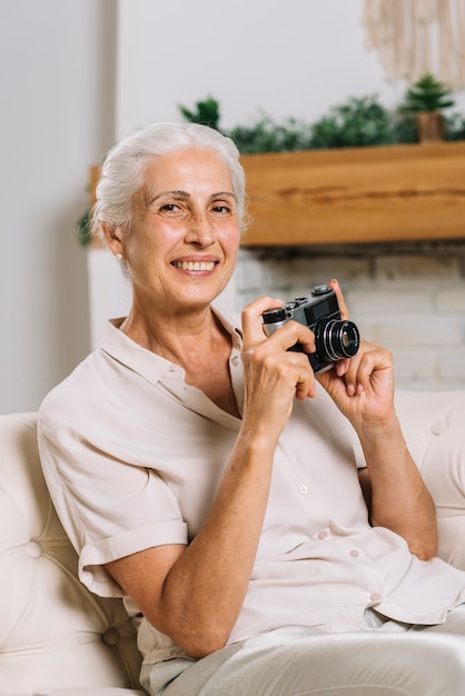 Ritratto della donna sorridente che si siede sulla macchina fotografica della holding del sofà