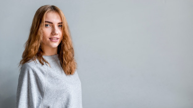 Portrait of a smiling woman standing against grey wall looking at camera