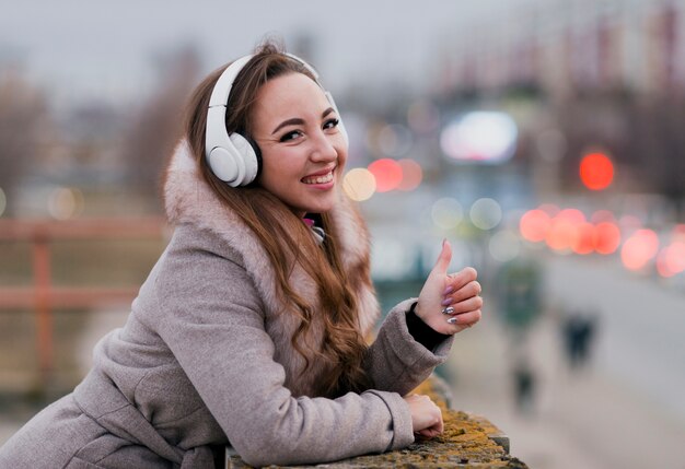 Portrait of smiling woman with headphones on roof showing hand sign