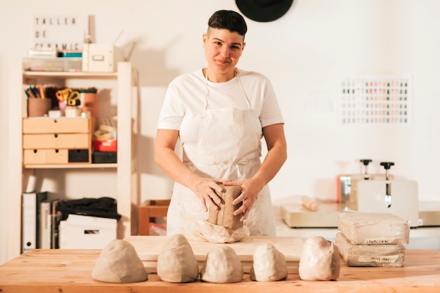 Free photo portrait of a smiling woman with kneaded clay in the workshop